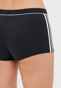 Calças de desporto pretas com riscas brancas laterais, apresentando um tecido liso e elástico e uma cinta de cor contrastante.