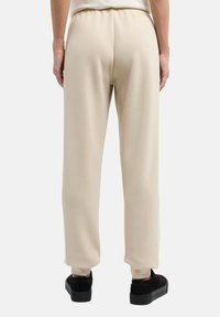 Ljust beige vida sweatpants med elasticitet i midjan och slät yta, kombinerat med svarta mockaskor och en subtil ribbad detalj vid anklarna.