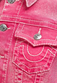 Różowa tkanina dżinsowa z białymi szwami i metalowym wykończeniem, z dwiema kieszeniami prezentującymi unikalne hafty oraz ozdobne wzory szycia.