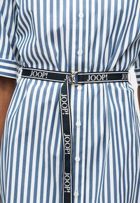 Μπλε και λευκό φόρεμα με κάθετες ρίγες και κουμπιά, με κοντά μανίκια, εφαρμοστό στη μέση με μαύρη ζώνη JOOP! με διπλή αγκράφα.