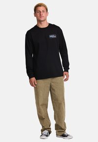 Black long-sleeve shirt with a logo detail on the left chest, paired with light brown corduroy pants and black sneakers.
