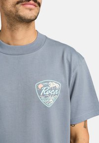 Lichtblauwe katoenen t-shirt met een driehoekig embleem van palmbomen, golven en een zon, bedrukt in pastelkleuren. Klassiek crewneck ontwerp.