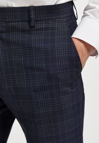 Marineblau karierte Hose mit feinem Karomuster, aus strukturiertem Stoff, mit geradem Schnitt und seitlichen Taschen. Entworfen für eine taillierte Passform.