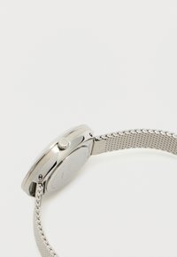 Ρολόι με ασημένιο μεταλλικό λουρί, στρογγυλή μεταλλική κάσα, λείο γυαλισμένο φινίρισμα και πλευρικό κορώνα για ρύθμιση. Μινιμαλιστικός σχεδιασμός με καθαρές γραμμές.