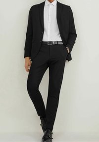 Svart kostym med figursydd jacka och byxor, vit skjorta med krage, svart bälte och svarta ankelskor med spännen. Ren design och skräddarsydd passform.
