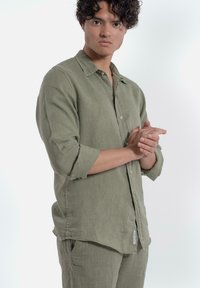 Licht olijfgroene linnen blouse met lange mouwen opgerold, knoopsluiting aan de voorkant en een zachte textuur, gecombineerd met bijpassende broek.