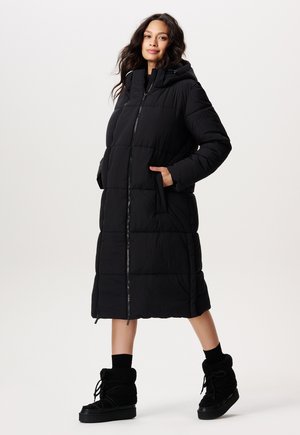 Schwarzer langer Daunenmantel mit Kapuze, Frontreißverschluss und Seitentaschen. Verfügt über gesteppte Paneele und eine lässige Passform. Kombiniert mit schwarzen Fleece-Stiefeln.