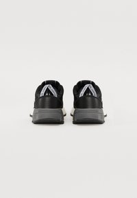 Black athletic shoes with a textured upper, featuring a gray rubber sole and contrasting white accents on the heel and logo.