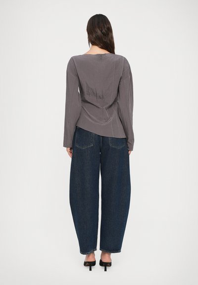Maglia grigia a manica lunga con scollatura circolare e cuciture decorative, abbinata a jeans denim blu scuro a gamba larga e scarpe con tacco nere.
