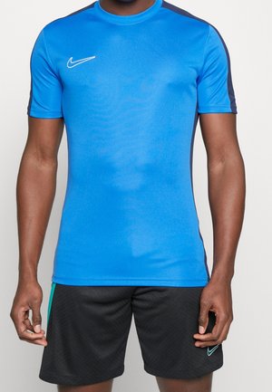 Mężczyzna w niebiesko-czarnej sportowej koszulce Nike z krótkim rękawem i czarnych szortach Nike na jednolitym tle.