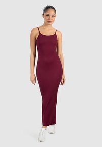 Burgunderrotes Maxikleid mit dünnen Trägern, figurbetonter Silhouette, dehnbarem Material, glatter Textur, getragen mit weißen Sneakers.