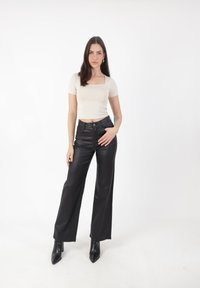 Top ajustado de cuello cuadrado en crema y pantalones anchos de imitación cuero negro de cintura alta. La modelo lleva botas de tobillo de punta negra. Fondo blanco liso.