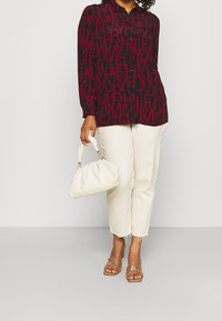 Rood en marineblauw patroon shirt met grote letters, beige cropped jeans, crèmekleurige handtas en sandalen met doorzichtige banden.