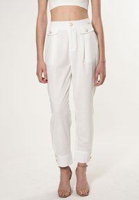 Witte high-waisted broek met twee frontzakken en gouden knopen. De stof lijkt lichtgewicht met een gladde textuur. Heeft omgeslagen mouwen.