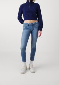 Marinblå kort tröja med hög krage, ihopkopplad med ljusblå smaljeans. Vita sneakers och vita strumpor kompletterar outfiten.