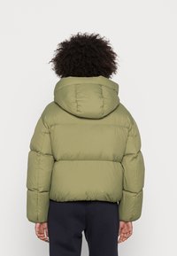 Giacca a vento verde oliva con cappuccio, design trapuntato e polsini elastici. Texture morbida con cappuccio arrotondato, vista da dietro.