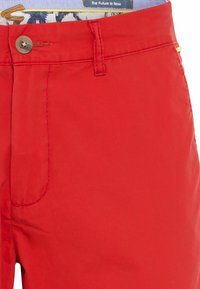 Shorts en coton rouge avec une fermeture à un bouton, une poche avant, une texture lisse et une ceinture intérieure à motif contrasté.