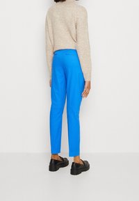 Niebieskie, elastyczne spodnie o tapered designie. Noszone z jasnobeżowym, teksturowanym swetrem i czarnymi butami na platformie.