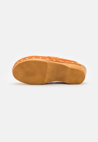Sandale à plateforme en suede orange avec une semelle texturée, ornée de clous blancs proéminents sur le bord et d'un design à bout arrondi.