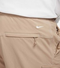 Beige shorts i mjukt tyg, med en sydd ficka, snörningsdetaljer och en vit Nike-swoosh-logga på baksidan.