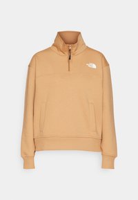 Sweat-shirt beige The North Face avec col montant, demi-fermeture éclair, manches longues, poches kangourou et logo sur la poitrine gauche.