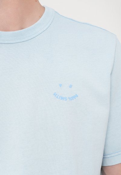 Világoskék pamut póló rövid ujjakkal, bal mellen kis kék hímzett mosolygós arc és "Paul Smith" felirat található.