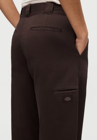 Braune Cargo-Hose mit glatter Textur, Seitentaschen und einem aufgenähten Logo am Oberschenkel. Gürtelschlaufen an der Taille, mit einer maßgeschneiderten Passform.