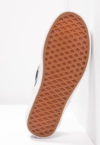 Semelle de basket blanche avec un motif hexagonal, une semelle extérieure en caoutchouc brun et un côté blanc propre. Texturée pour l'adhérence et la stabilité.