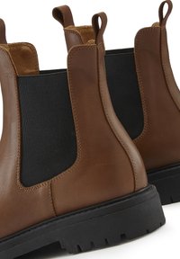 Brown leather ankle boots with elastic side panels, textured black fabric, and a rugged black rubber sole. Stitched detailing visible.