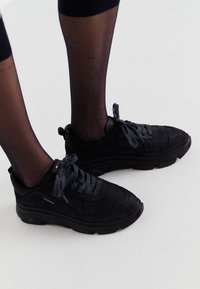 Baskets noires avec une finition en daim texturé et des semelles en caoutchouc. Présentent un design à lacets et un logo sur le côté.