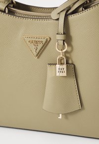 Borsa in materiale testurizzato verde oliva con hardware dorato, caratterizzata da un logo triangolare e un piccolo charm a forma di lucchetto con dettaglio "EST 1981".