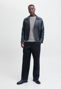 Veste de motard en cuir noir sur un pull côtelé gris, associée à un pantalon noir et des chaussures brillantes. Design simple avec un minimum de matériel.