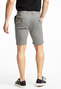 Pantaloncini grigi in cotone con vestibilità slim, orli arrotolati, due tasche posteriori e cintura piatta. Abbinati a sneakers nere.