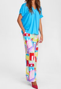 Top blu, a maniche corte abbinato a pantaloni colorati e fantasia con case astratte in diverse tonalità. Tacchi rosa completano l'outfit.
