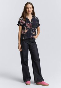 Navy floral shirt with short sleeves and a v-neck, paired with dark wide-leg jeans and pink sneakers. Smooth fabric with vibrant patterns.