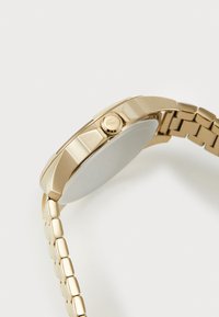 Goldfarbene Armbanduhr mit runder Gehäuseform, strukturiertem Lünette und einem Gliederarmband mit polierten und gebürsteten Oberflächen.