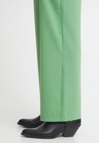 Nogi ubrane w jasnoniebieskie szerokie spodnie i czarne skórzane botki na niskim obcasie z szpiczastym noskiem.