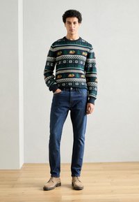 Gebreid truitje in donkergroen met een patroonontwerp van sneeuwvlokken en dieren, gecombineerd met blauwe spijkerbroeken en beige veterschoenen.
