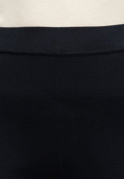 Μαύρο πλεκτό παντελόνι με ψηλή μέση και ορατές ραφές σε μπεζ επιφάνεια.