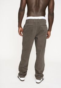 Grå bomuldsbukser med en lige pasform, der har en hvid talje, to baglommer og let struktur. Båret med sorte og hvide sneakers.