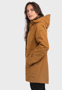 Braune wasserdichte Jacke mit Kapuze, Fronttaschen und einem eleganten Design. Strukturierter Stoff, moderne Passform und dezentes Logodesign am Ärmel.