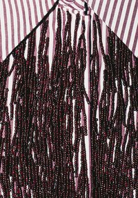 Blusa a righe con dettaglio di frange nere realizzate con decorazioni simili a perline. Il colletto è ampio con righe verticali a contrasto.