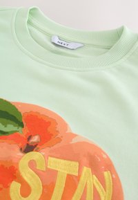 Svetlozelená bavlnená mikina s dizajnom pomaranča a žltým vyšitým textom. Zaoblený výstrih a detail s rebrovaným lemovaním.