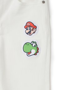 Tela de denim blanca con dos parches bordados coloridos: uno de Mario con gorra roja y bigote, y otro de Yoshi en verde con acentos blancos.