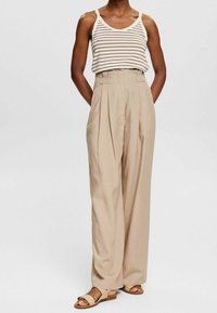 Beige, högmidjade byxor med vida ben, veck och sidofickor, i kombination med en vit och brun randig linne. Neutrala sandaler.