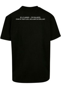 Camiseta de algodón negra con mangas cortas y cuello redondo. Texto en la parte posterior: "SÉ UN FLAMENCO – MANTENTE EN EQUILIBRIO, PERMANECE CON TU MANADA Y SÉ SIEMPRE BRILLANTE."