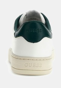 Sneaker in pelle bianca con un accento verde scuro sul tallone. Presenta il nome del brand in rilievo e una suola beige strutturata.