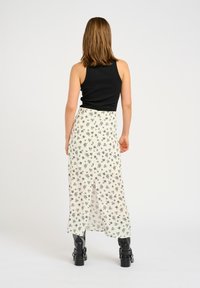 Top nero senza maniche abbinato a una gonna maxi fluida di colore crema con motivo floreale; donna che indossa stivali neri fino al ginocchio.