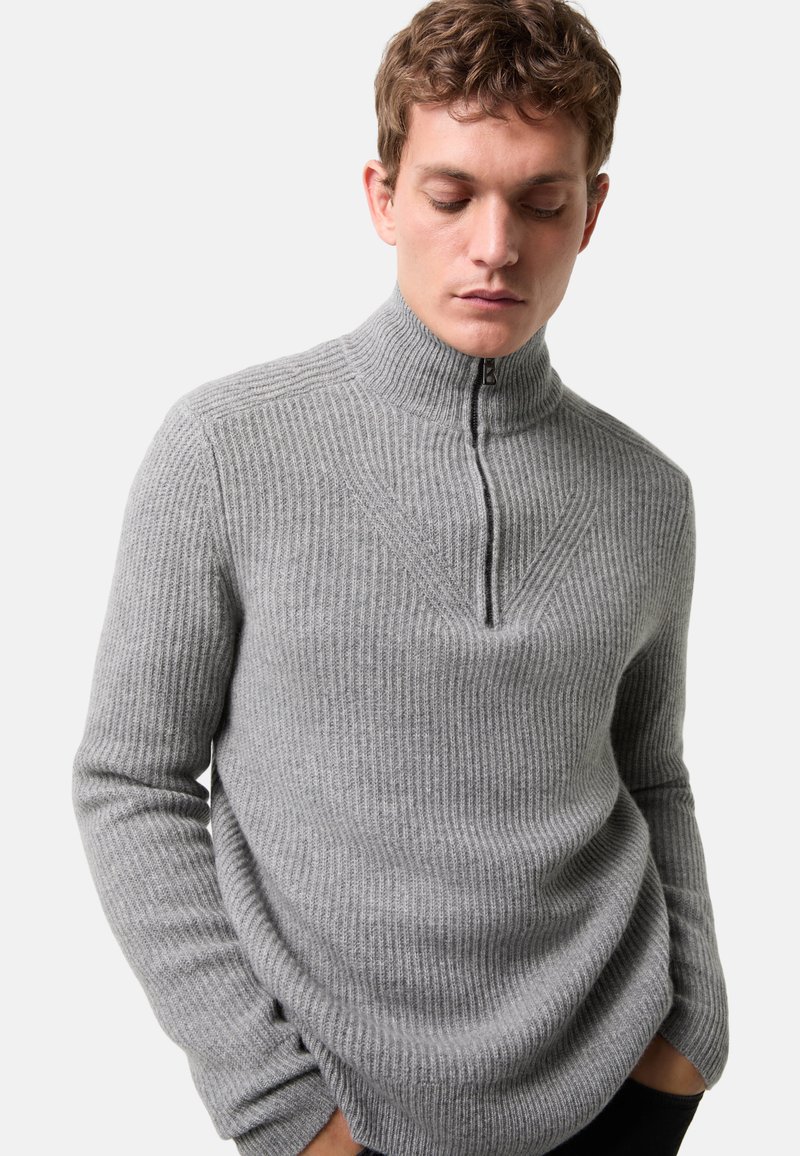 Grau gerippter Pullover mit hohem Kragen und halbem Reißverschluss. Weicher Stoff, taillierte Silhouette mit einer V-förmigen Nahtdesign an der Brust.