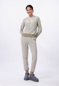 Felpa beige chiara a maglia con cordini, abbinata a pantaloni coordinati. Stivaletti grigi alla caviglia completano l'ensemble casual. Tessuto morbido, vestibilità rilassata.